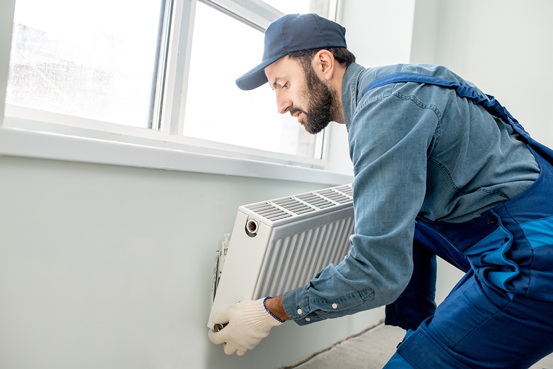 Workman mounting water heating radiator near the window in the white renovated living room