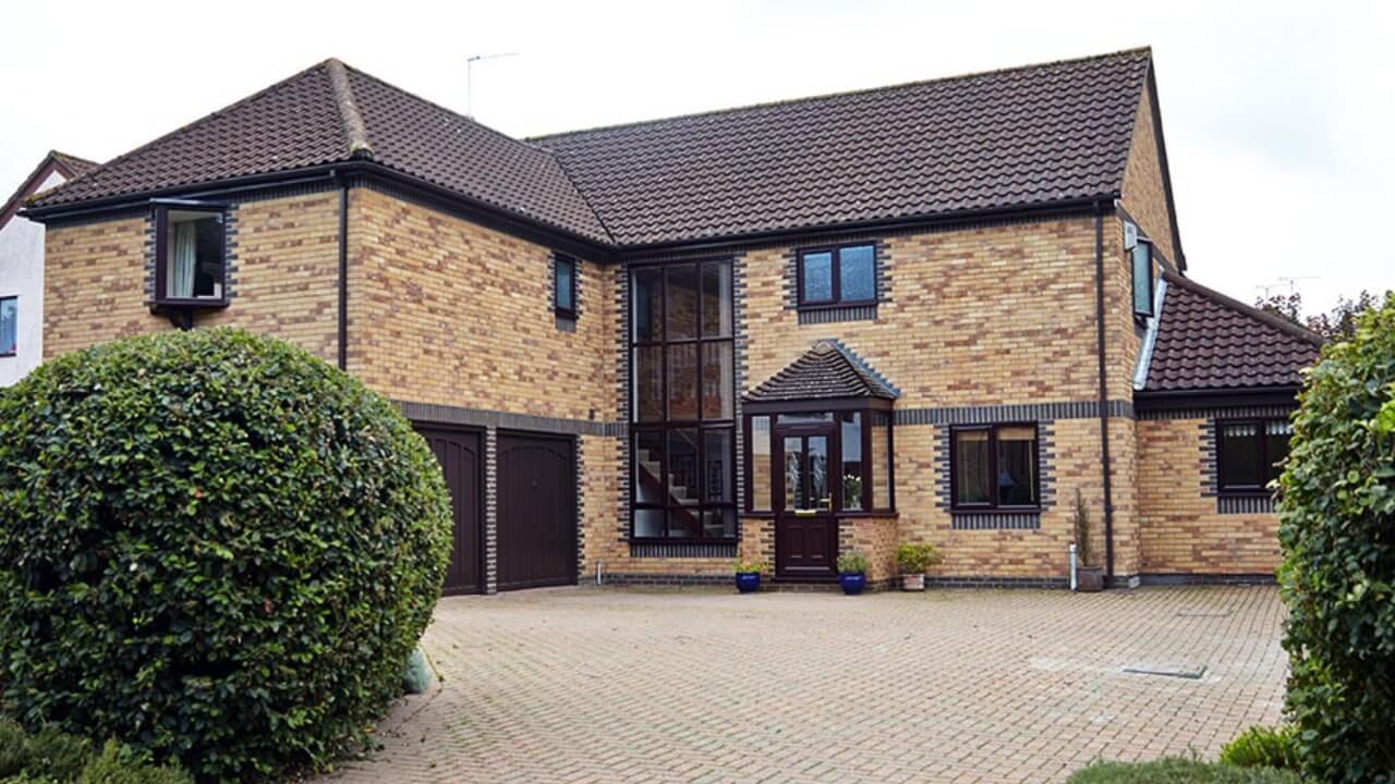 Anglian vs Everest. Anglian dark brown uPVC double glazing windows installed across a whole house, including a large, multi-story arrangement of windows.