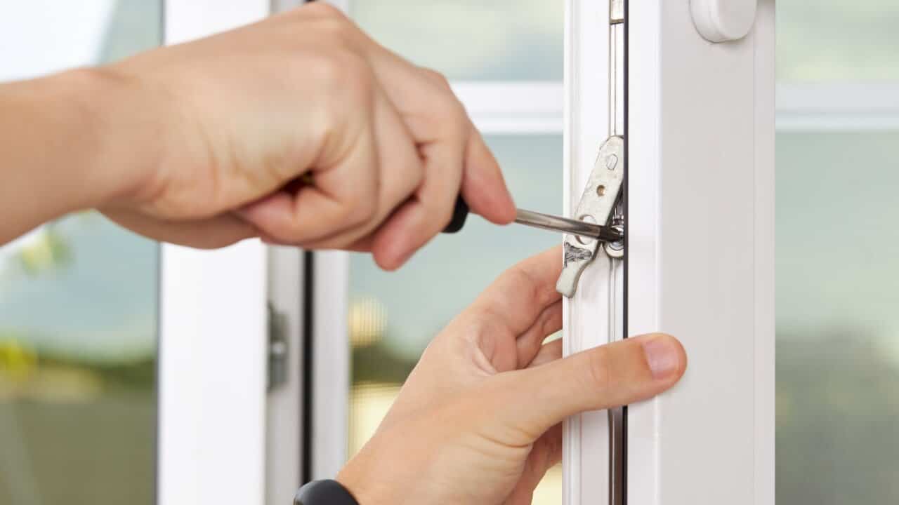 A person adjusting white uPVC window indoors using a screwdriver to adjust the height of the window in the frame.