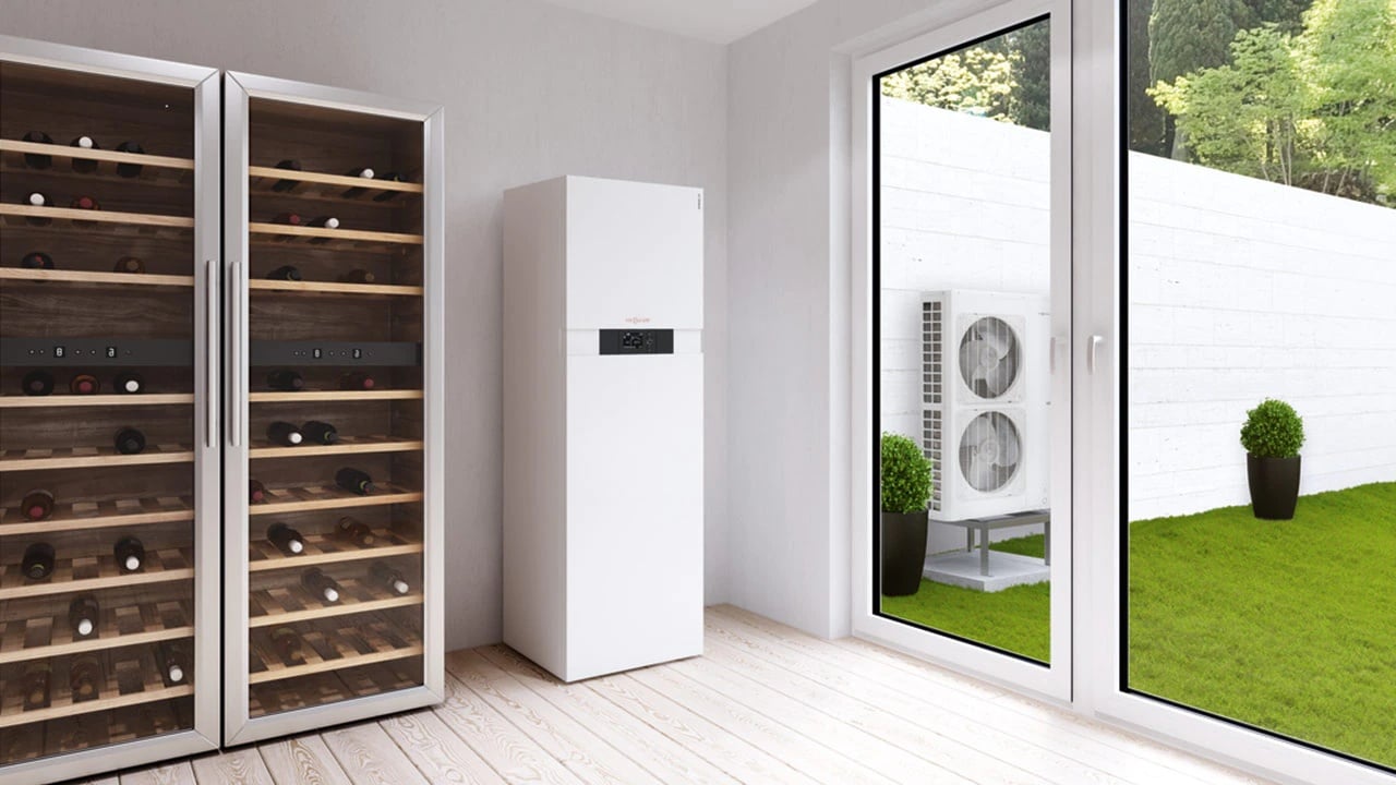 A Viessmann Vitocal 100-A air source heat pump installed outside a house with a hot water tank installed inside the house.
